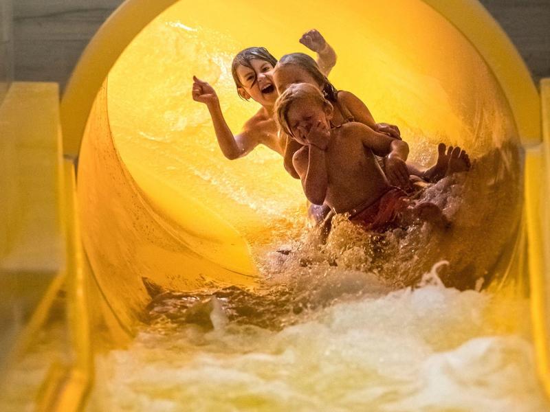 Zwei Kinder rutschen lachend eine gelbe Wasserrutsche hinunter im Freibad.