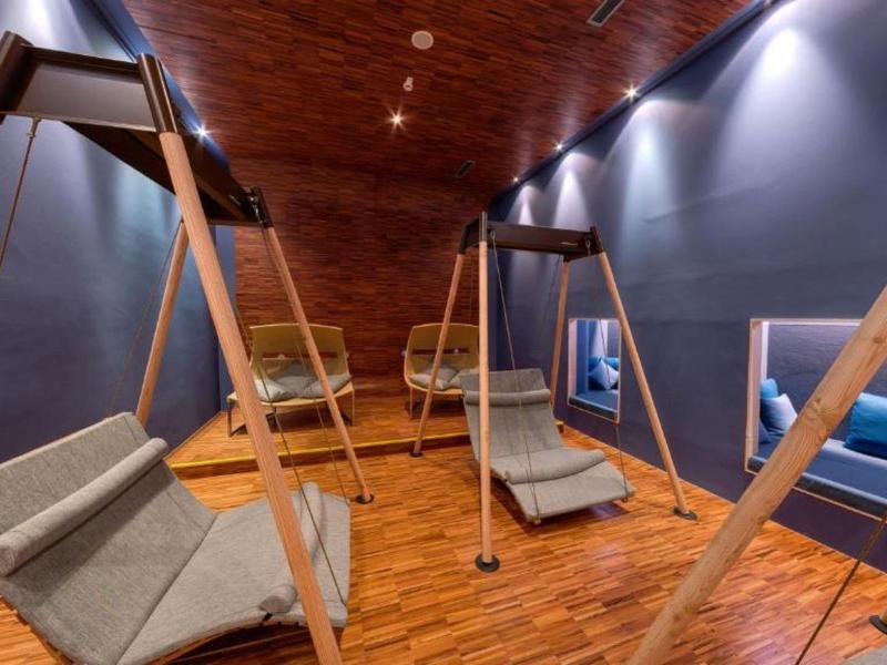 Moderner Raum mit hängenden Sesseln, dunklen Wänden und Holzdecke mit eingebauter Beleuchtung.