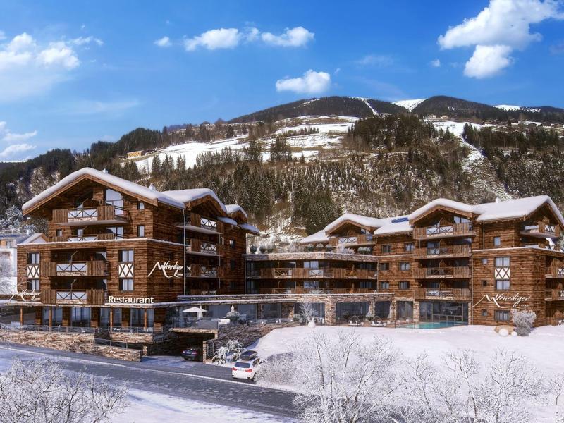 Große Holzgebäude mit Balkon in verschneiter Berglandschaft unter blauem Himmel.