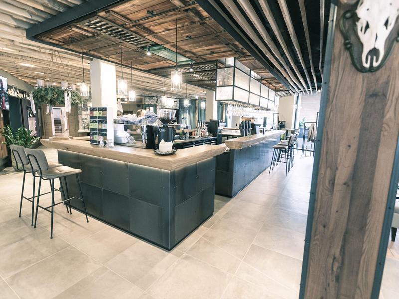 Moderner Kaffeehaus-Innenraum mit Holzsäule, Barhockern und Arbeitsfläche aus Holz und Metall.