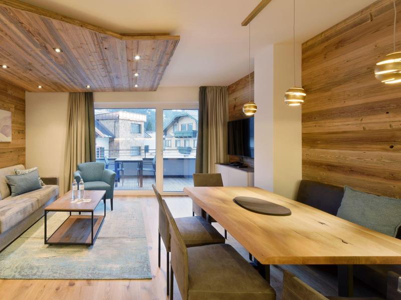 Modernes Wohnzimmer mit Holzwänden, großem Esstisch, Sofa, Sessel und bodentiefen Fenstern.