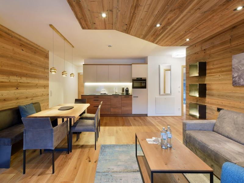 Modernes Wohnzimmer mit Holzwänden, grauem Sofa, blauem Sitzbereich und Esstisch mit Stühlen.