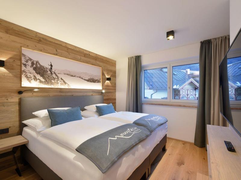 Gemütliches Schlafzimmer mit Holzwänden, großem Bett, Panoramabild und Winterlandschaft draußen.