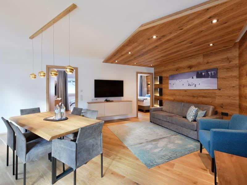 Moderner Wohn- und Essbereich mit Holzwänden, grauem Sofa, blauem Sessel und Holztisch.