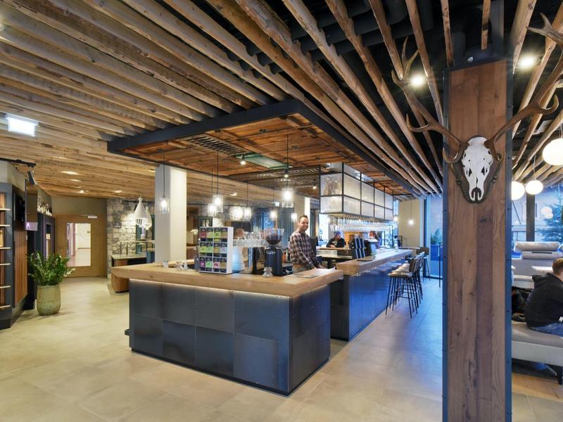 Modernes Hotelbarinterieur mit Holzdecke, Tresen und Sitzbereich bei Tageslicht.