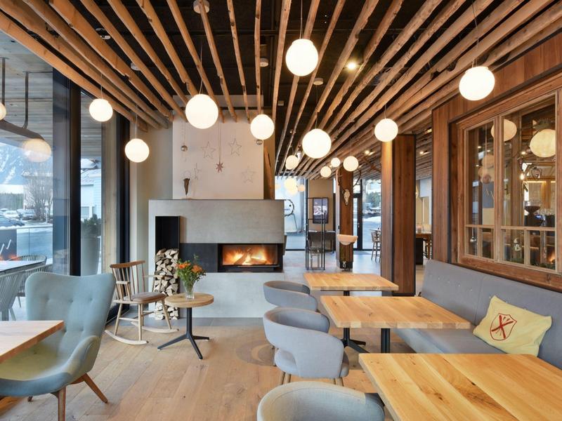 Modernes Café mit Holzdecken, runden Hängelampen, gemütlichen Sesseln und Holztischen.