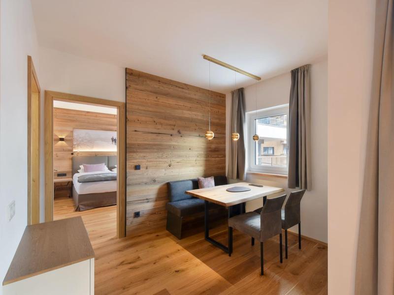 Moderner Essbereich mit Holzfußboden, Tisch, zwei Stühlen, Eckbank und Blick ins Schlafzimmer.