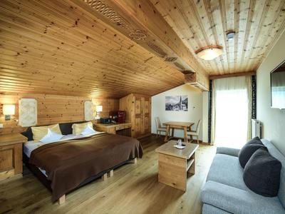 Gemütliches Schlafzimmer mit Holzwänden, Doppelbett, Sofa, Tisch und großem Fenster mit Vorhang.