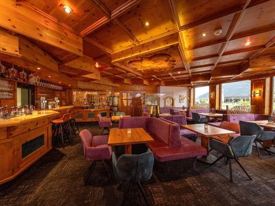 Gemütlicher Hotelbarbereich mit Holzbalkendecke, gepolsterten Sitzbänken und großen Fenstern.