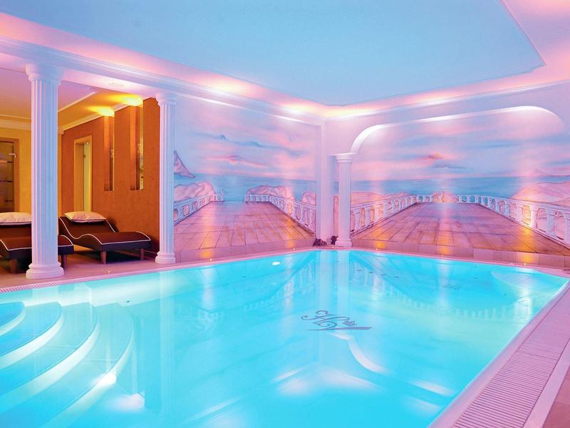 Hell beleuchteter Innenpool mit Säulen und Wandbildern von Sonnenuntergängen am Meer.