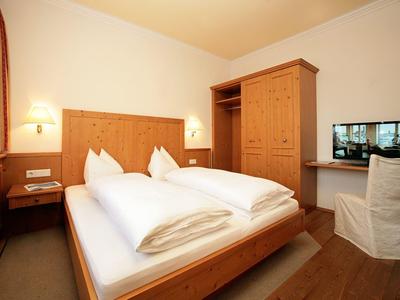 Gemütliches Schlafzimmer mit Doppelbett, Holzschrank, TV und warmem Licht, schlicht eingerichtet.