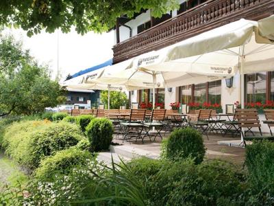 Außenbereich eines Cafés mit Tischen, Stühlen und Sonnenschirmen neben einem grünen Garten.