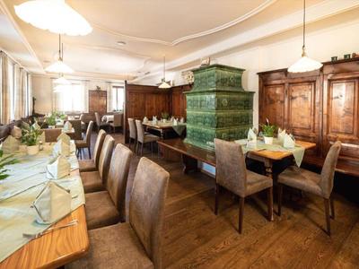 Gemütlicher Speiseraum mit Holzvertäfelung, Tischreihen und grünem Kachelofen