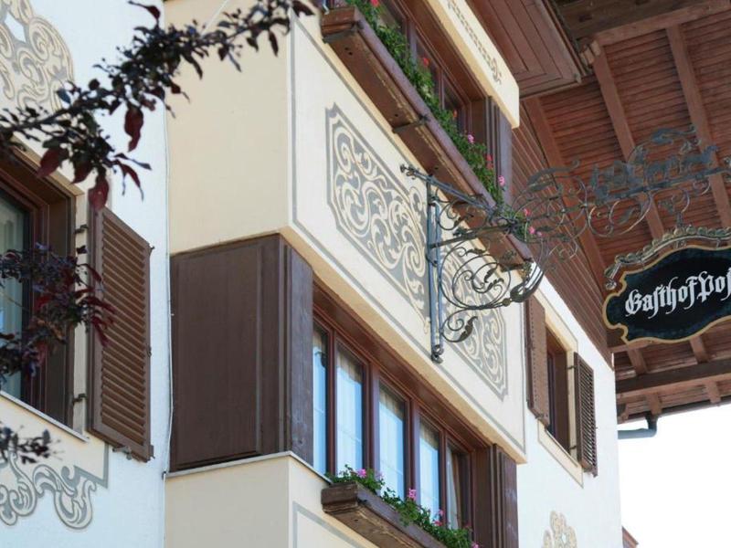 Fassadendetail eines Hauses mit verzierten Fensterläden, Blumenkästen und einem Schild "Gasthof Post".