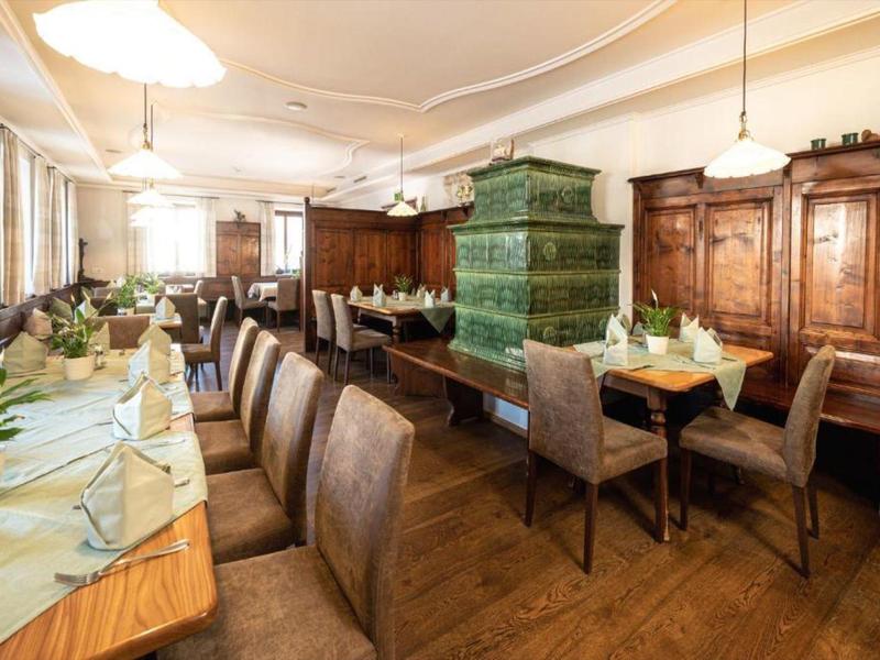 Gemütlicher Gastraum mit Holzmöbeln, grüner Kachelofen und gedeckten Tischen mit Blumen.