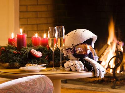 Romantische Szene mit Kerzen, Sektgläsern und Händen vor einem Kaminfeuer im gemütlichen Zimmer.