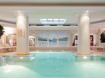 Helles Schwimmbad mit Säulen, großen Fenstern und entspannenden Liegestühlen im modernen Raum.