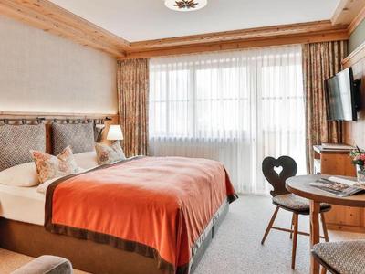 Gemütliches Hotelzimmer mit Doppelbett, Holzmöbeln, orangefarbenem Bettüberwurf und großen Fenstern.