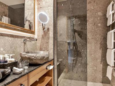 Modernes Badezimmer mit grauen Steinwänden, Glasdusche, Steinwaschbecken und Holzunterschrank.