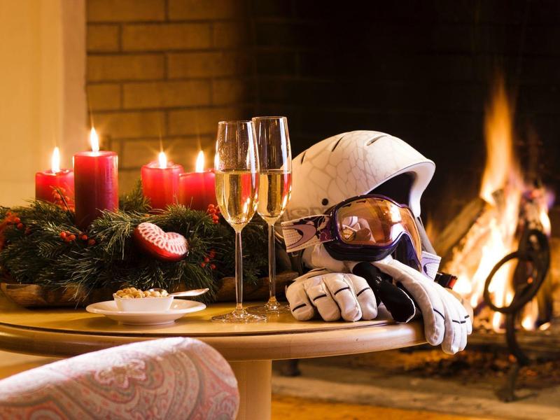 Astronaut in Raumanzug sitzt an Tisch mit Kerzen, Sektgläsern vor Kaminfeuer.