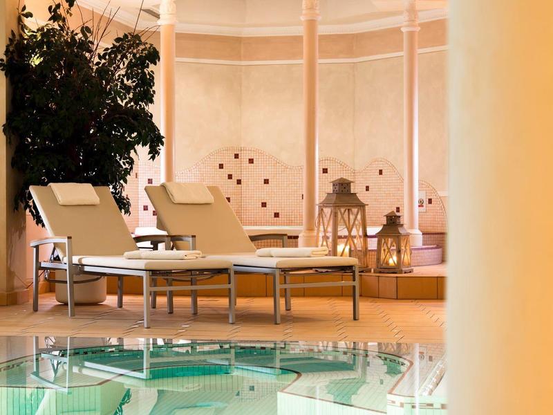 Innenraum mit Pool, zwei weißen Liegestühlen, Pflanzen, warmem Licht und Dekoration an Wänden.