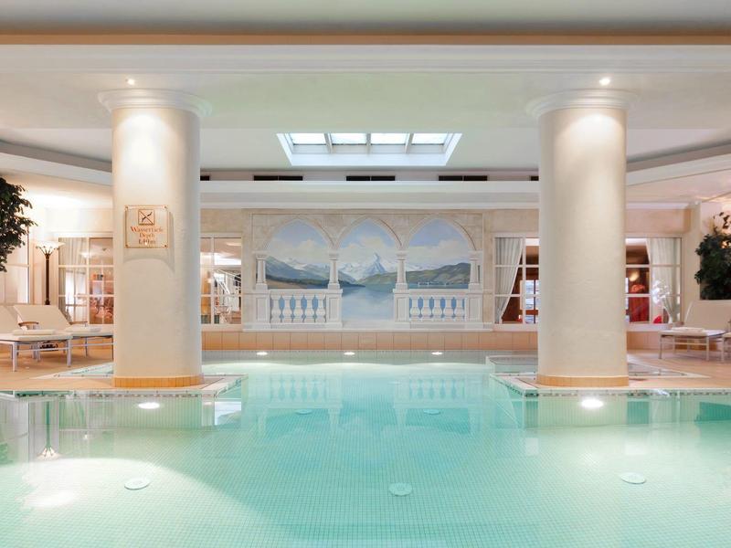 Helles Schwimmbad mit Säulen, großen Fenstern und entspannenden Liegestühlen im modernen Raum.