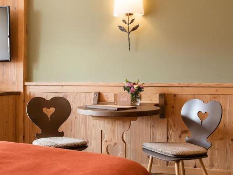 Gemütliches Zimmer mit Holzmöbeln, Herzstuhl-Design und warmem Licht an grünlicher Wand.