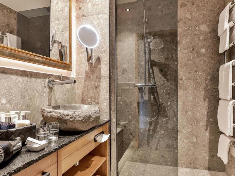 Modernes Badezimmer mit grauen Steinwänden, Glasdusche, Steinwaschbecken und Holzunterschrank.