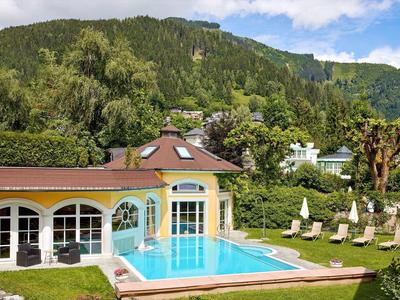 Haus mit kleinem blauen Pool, Sonnenschirmen und grünen Bergen im Hintergrund.