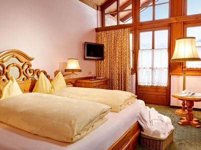 Gemütliches Hotelzimmer mit Holzdecke, zwei Betten, gelben Bettdecken und roten Sesseln.