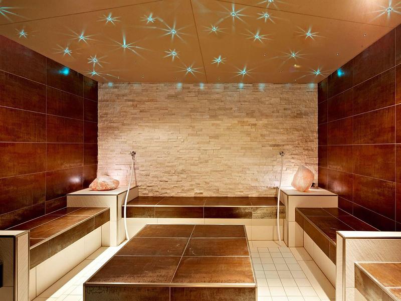 Modern gestalteter Dampfraum mit braunen Holzpaneelen, Fliesenboden und Sternenlichtdecke.