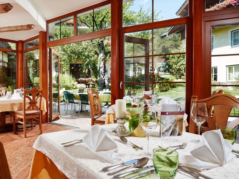 Gemütliches Restaurant mit großen Fenstern, eingedeckten Tischen und Blick in grünen Garten.