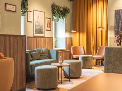 Accogliente lounge dell'hotel con poltrone, sgabelli e piante vicino alle tende.