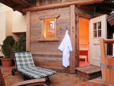 Gemütliche Sauna mit Holzwand, Liegestuhl, Pflanzen und geöffnetem Türlicht.