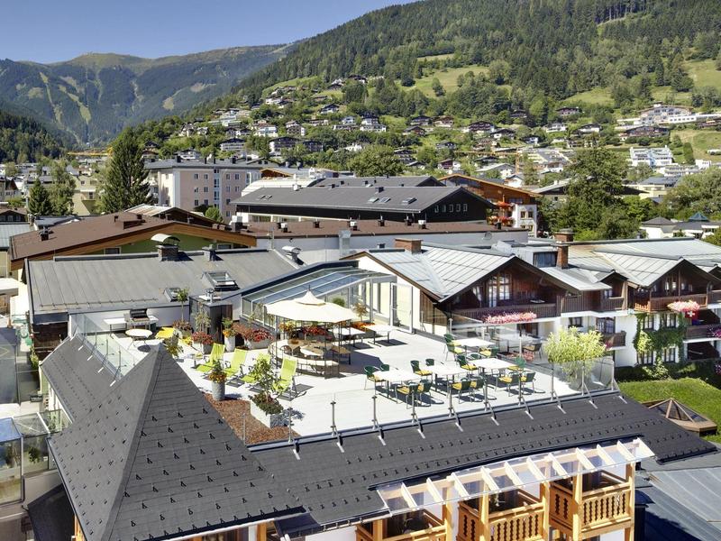 Bergdorf mit Holzhäusern, grünen Hügeln und klarem blauem Himmel im Hintergrund.