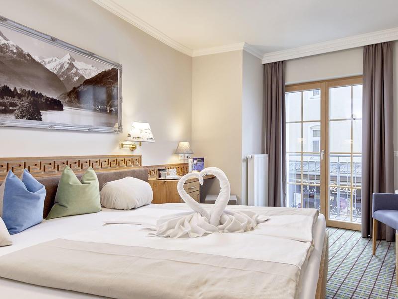 Helles Schlafzimmer mit großem Bett, weißen Handtüchern in Herzform und Bergblick-Fotografie an der Wand.