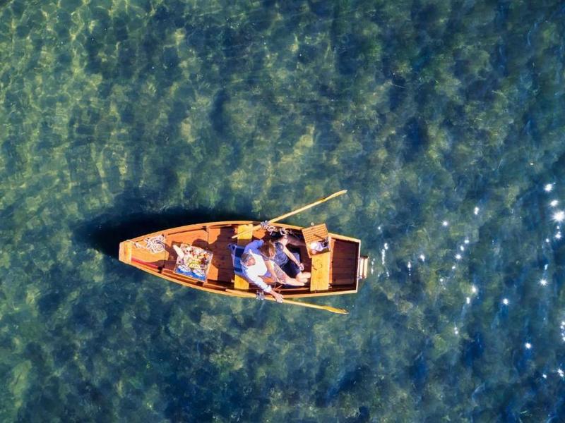 Kleines Boot auf klarem, grün-blauem Wasser mit zwei sitzenden Personen und Sonnenschein.
