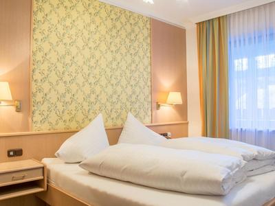 Gemütliches Schlafzimmer mit Holzbett, weißen Bettdecken, Wandlampen und gemustertem Wandpaneel.