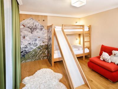 Kinderzimmer mit Hochbett und Rutsche, rotem Sofa und Berglandschaftswanddekoration.