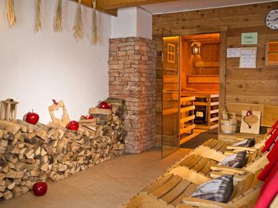 Gemütlicher Saunaraum mit Holzbänken, Holzstapel und offenem Durchgang zur Sauna.