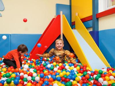 Kind spielt fröhlich im Bällebad vor zwei bunten Rutschen in einem hellen Spielzimmer.