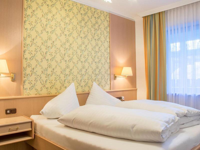 Gemütliches Schlafzimmer mit Holzbett, weißen Bettdecken, Wandlampen und gemustertem Wandpaneel.