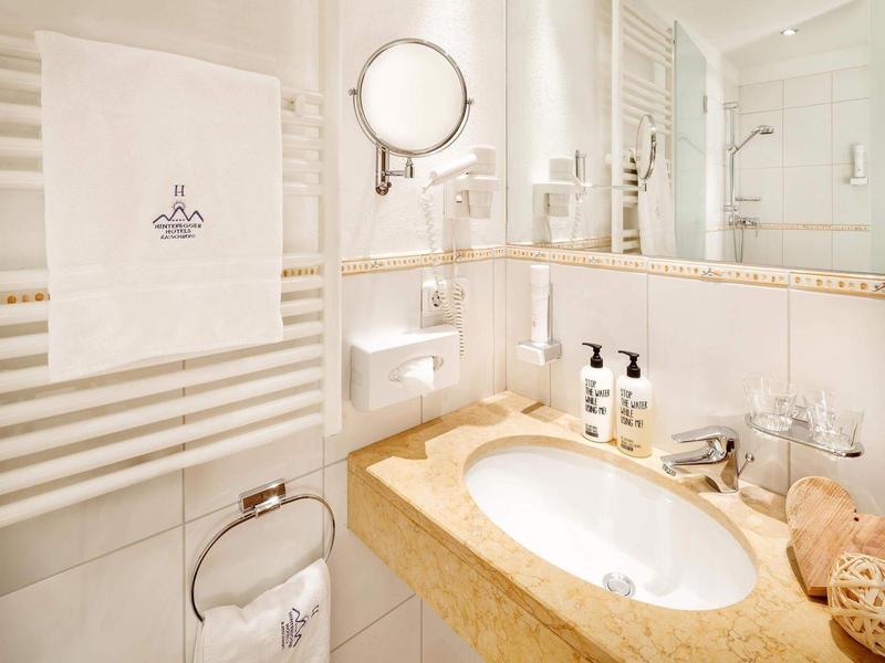 Helles Badezimmer mit weißem Handtuch, großem Spiegel und Waschbecken in cremefarbener Ablage.