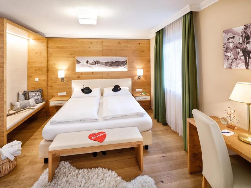 Modern eingerichtetes Schlafzimmer mit Doppelbett, Holzvertäfelung, Schreibtisch und gemütlicher Beleuchtung.