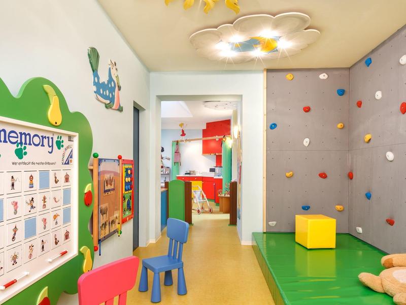 Bunter Kinderspielraum mit Kletterwand, Matten, bunten Stühlen und wandmontierten Spielen.