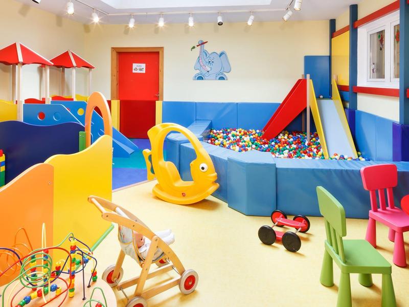 Bunter Kinderspielraum mit Rutsche, Bällebad, Spielzeugautos und kleinem Tisch mit Stühlen.