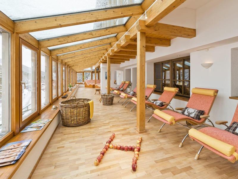 Heller Holzraum mit großen Fenstern, Liegestühlen und Körben, ruhige Atmosphäre.