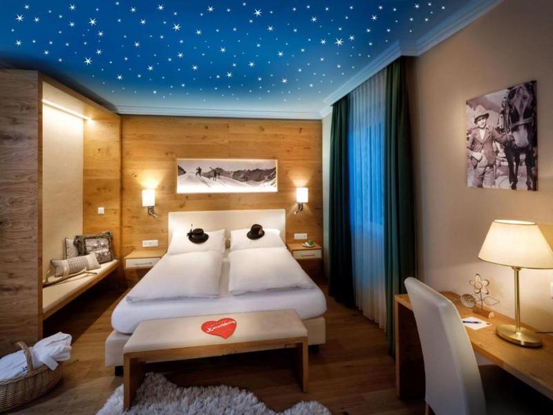 Gemütliches Schlafzimmer mit Holzwänden, Sternenleinendecke, Doppelbett und Schreibtisch mit Lampe.