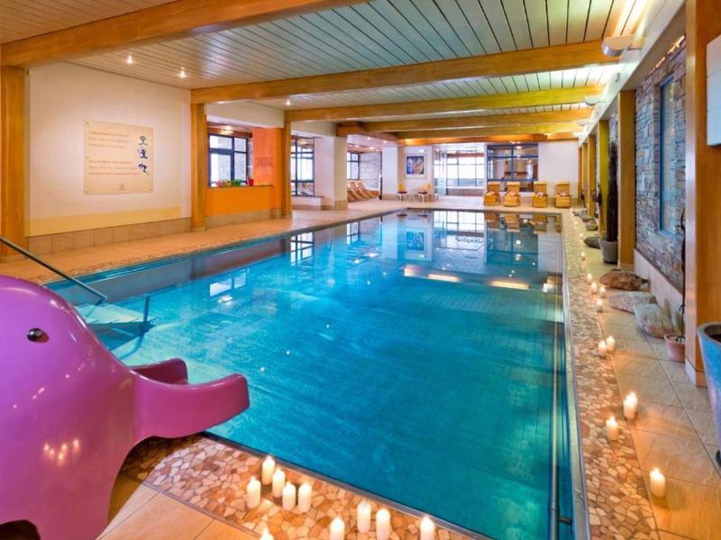 Innenraum mit einem großen Schwimmbad, Holzwänden, Glasfenstern und einem pinken Kinder-Wasserrutsche.