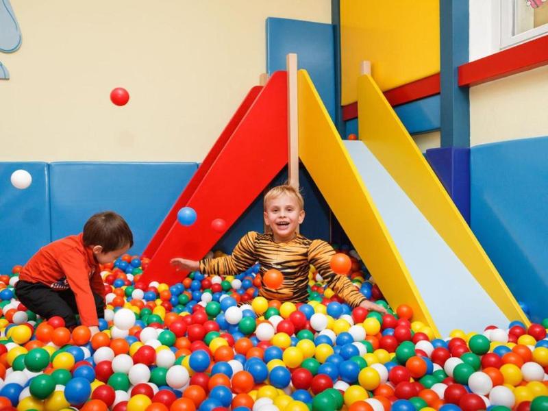 Kind spielt fröhlich im Bällebad vor zwei bunten Rutschen in einem hellen Spielzimmer.